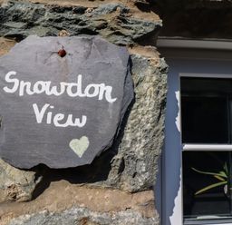 A stone wall with a slate sign reading Snowdon View next to a white-framed window with a plant inside at Snowdon View Harlech
