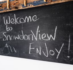 A blackboard with welcome to Snowdon View Enjoy written in chalk and a drawing of mountains at Snowdon View Harlech