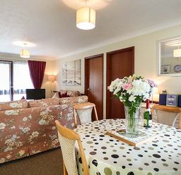 A living room with floral sofas a dining table with flowers on it and a sideboard with a mirror at Chy Lowenna Rosecraddoc Holiday Village near Liskeard