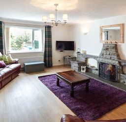 A living room with a red sofa and cushions a purple rug wooden coffee table a stone fireplace and a wall-mounted TV at Simdda Wen Cottage in Llanddona near Beaumaris