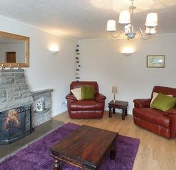 A living room with two leather armchairs a fireplace a wooden coffee table and a purple rug at Simdda Wen Cottage in Llanddona near Beaumaris