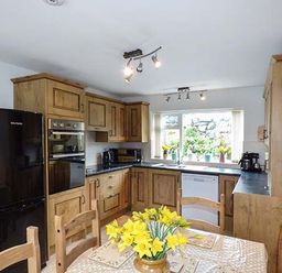 A kitchen with wooden cabinets black refrigerator and a table with yellow flowers at Simdda Wen Cottage in Llanddona near Beaumaris