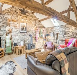 A living room with stone walls exposed wooden beams wood-burning stove and various seating at Berts Cottage Heights near Appleby-in-Westmorland