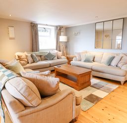 A living room with beige sofas a wooden coffee table a floor lamp and a large wall mirror at Is Y Deri in Harlech