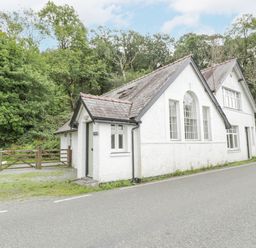 A white house with multiple windows and a gated entrance by the road at Is Y Deri in Harlech