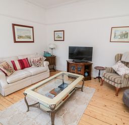 A living room with a sofa and armchair with cushions a glass coffee table a television on a stand and framed pictures on the walls at Iona 10 Palace Street East in Berwick-upon-Tweed