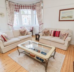 A living room with two beige sofas with cushions a glass coffee table and a window with curtains at Iona 10 Palace Street East in Berwick-upon-Tweed