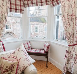 A window nook with a wooden bench and plaid cushions and floral curtains at Iona 10 Palace Street East in Berwick-upon-Tweed