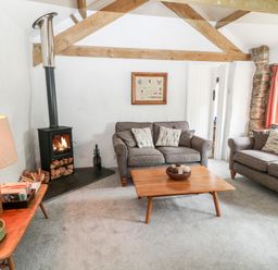 A living room with two gray sofas a wooden coffee table and a wood burning stove at Treverbyn Smithy in St Neot