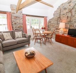 A living room with gray sofas a wooden coffee table a dining table with chairs and a TV on a wooden cabinet at Treverbyn Smithy in St Neot