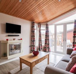 A living room with a wooden coffee table a grey sofa with cushions patterned curtains and a wall-mounted television at 22 Thirlmere in Troutbeck Bridge