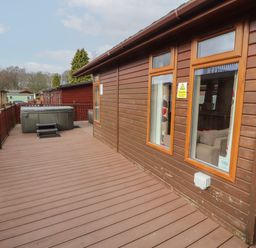 A deck with a fenced railing and a hot tub outside wooden cabins at 22 Thirlmere in Troutbeck Bridge