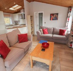 A living room with two sofas red cushions wooden coffee table and open kitchen at 22 Thirlmere in Troutbeck Bridge