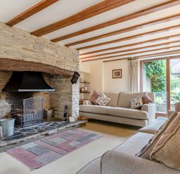 A living room with two sofas a stone fireplace and large window at West End Barn in Cleeve Prior near Evesham