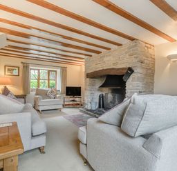 A living room with sofas a stone fireplace and wooden beams on the ceiling at West End Barn Cleeve Prior near Evesham