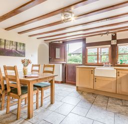 A kitchen with wooden cabinets a farmhouse sink dining table with chairs and an open door at West End Barn in Cleeve Prior near Evesham