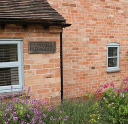 A brick wall of Pebworth Cottage with two windows flowers and a hanging flower basket at Pebworth near Stratford-upon-Avon