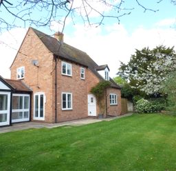 A brick house with a white framed glass extension and garden with grass and trees at Pebworth Cottage in Pebworth near Stratford-upon-Avon