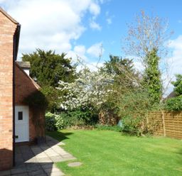 A garden with a lawn trees and shrubs next to a brick house with a tiled patio at Pebworth Cottage in Pebworth near Stratford upon Avon
