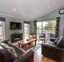 A living room with leather sofas a wooden coffee table sliding glass doors and a wall clock at Claife View Lodge in Troutbeck Bridge