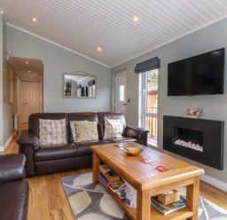 A living room with brown leather sofas a wooden coffee table a wall-mounted TV and a fireplace at Claife View Lodge in Troutbeck Bridge