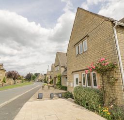 A row of stone houses along a street with flower pots on the pavement and climbing plants on the walls at Rosemary Cottage in Bourton-on-the-Water