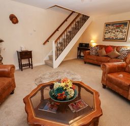 A living room with brown leather sofas a glass topped coffee table with flowers and a staircase in the background at Rosemary Cottage in Bourton-on-the-Water