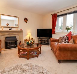 A living room with a fireplace a leather sofa and armchair a coffee table and a television at Rosemary Cottage in Bourton-on-the-Water