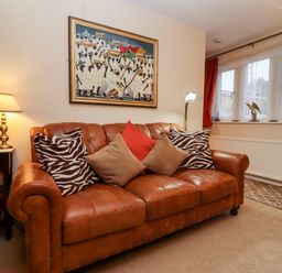A living room with a brown leather sofa with cushions and a side table with a lamp and books at Rosemary Cottage in Bourton-on-the-Water