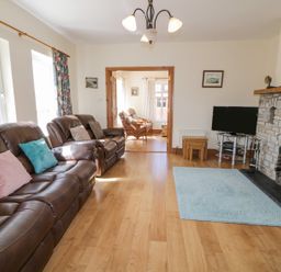 A living room with leather sofas cushions a stone fireplace a television and wooden flooring at Creeslough View in Creeslough near Glenveagh National Park County Donegal