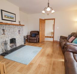 A living room with a stone fireplace leather armchairs and couch hardwood floors and a blue rug at Creeslough View Creeslough near Glenveagh National Park County Donegal