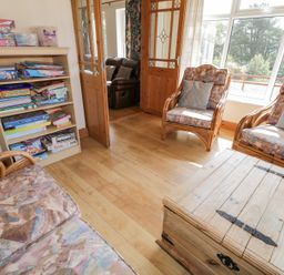 A sitting room with wooden furniture a bookshelf with board games and large windows at Creeslough View in Creeslough near Glenveagh National Park County Donegal