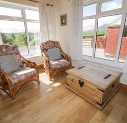 A sitting area with two wooden armchairs with patterned cushions a wooden chest and large windows at Creeslough View in Creeslough near Glenveagh National Park County Donegal