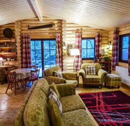 A living room with wooden walls chairs a table and a patterned rug at Wilderness Lodge in Stiperstones