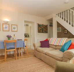 A living room with a beige sofa with colorful cushions a dining table with a blue checkered tablecloth and wooden chairs at Drover's in Sutton Mallet