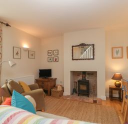 A living room with a wood burning stove a sofa a television and a dining table with a blue checkered tablecloth at Drover's in Sutton Mallet