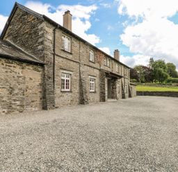 A stone building with multiple windows and chimneys next to a gravel driveway and green lawn at Buttermere in Sawrey near Hawkeshead