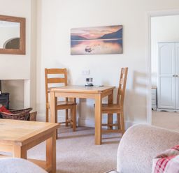 A dining area with two wooden chairs and a table near a fireplace with a wicker basket and a mirror above at Buttermere Sawrey near Hawkeshead