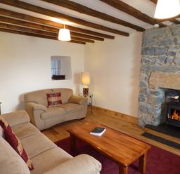 A living room with beige sofas a wooden coffee table and a stone fireplace at Ffynnon Gower in Llangower near Bala