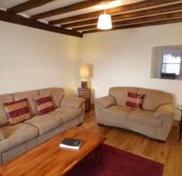 A living room with two beige sofas a wooden coffee table wooden beams on the ceiling and two lamps at Ffynnon Gower in Llangower near Bala