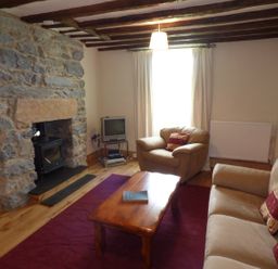 A living room with stone fireplace wooden ceiling beams and beige armchairs at Ffynnon Gower in Llangower near Bala