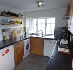 A kitchen with wooden cabinets black countertops tiled backsplash and appliances at Ffynnon Gower in Llangower near Bala
