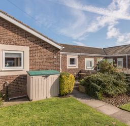 A brick residential building with windows a small garden shed and shrubs at Rock Rose Beadnell