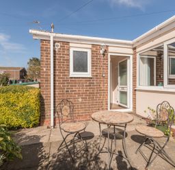 An outdoor patio with a round table and two chairs next to a brick house with an open door at Rock Rose in Beadnell