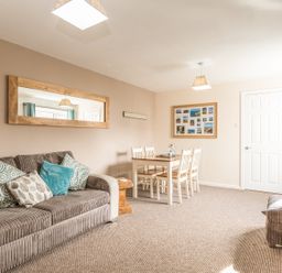 A living room with a sofa and dining table next to a white door at Rock Rose in Beadnell