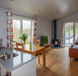A living room with a kitchen sink wooden dining table chairs a TV wood stove and leather sofa at Shepherd Lodge in Allithwaite near Grange-over-Sands