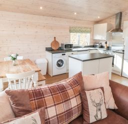 A kitchen and dining area with wooden table white chairs washing machine and brown sofa at Thorntree Lodge in Rowsley