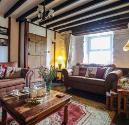 A living room with brown sofas a wooden coffee table and flowers in a vase at Hendy Cottage in Llanbedr near Harlech