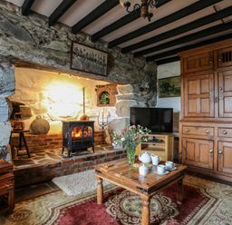 A living room with stone walls a fireplace wooden furniture and a television at Hendy Cottage in Llanbedr near Harlech