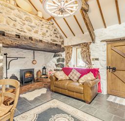 A living room with a leather sofa and cushions near a wood stove fireplace and wooden door at Y Becws in Llanbedr near Harlech